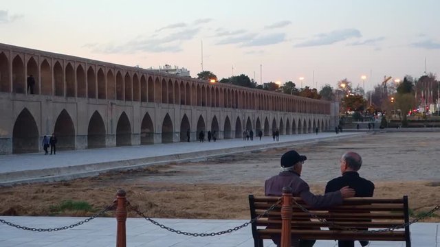 Two old men fraternising on a bench near the bridge with the dry Zayanderud river. Isfahan, Iran.