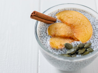 Chia seed pudding with slices peach and pumpkin seeds on a light table.