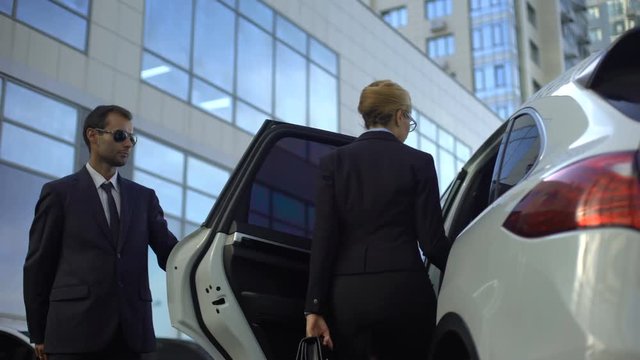 Personal driver waiting for boss on parking lot, helping her to get into car