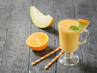 Melon smoothie with cocktail tubes and orange on a wooden table.