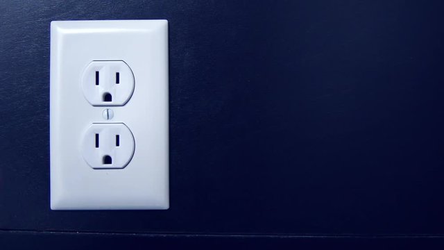 Light turns on and off at night as a cord is plugged into the bottom outlet and removed from an American electrical socket, copy space right