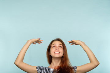 happy joyful smiling woman pretending to hold smth above her head with hands. virtual message or object pressing down on young beautiful brown haired girl. advertising space on blue background. - Powered by Adobe