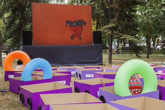 Children watch cartoons in an open cinema in the park. The seats are made of cardboard boxes, the back of seats from inflatable cylinders