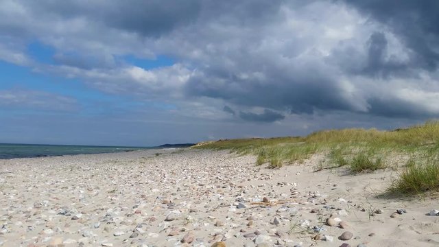 Liseleje Beach by the Tisvilde forest and coastal area on the Danish island of Zealand. Pristine sunny beach with dramatic clouds coming in. Change of weather. Scattered stones. Sand dunes with reeds.