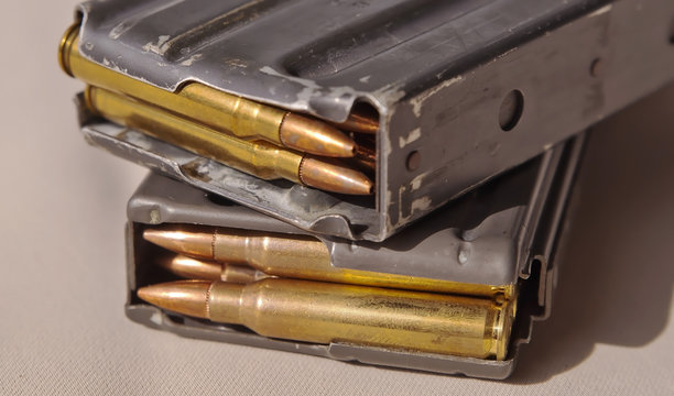 Two metal rifle magazines, one stacked upon the other, loaded with .223 caliber bullets