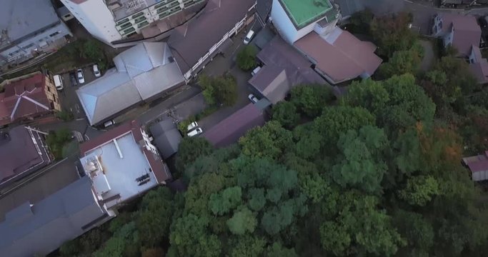 Drone flying forward towards a hot spring pool high above buildings while panning up in Kusatsu Onsen in Gunma Prefecture, Japan