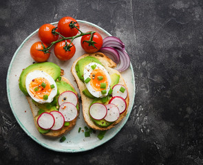 Healthy breakfast, Toasts with avocado, egg, radish, sweet onions and tomatoes, Diet food, On a darkbackground, Selective focus, Copy space, Top view