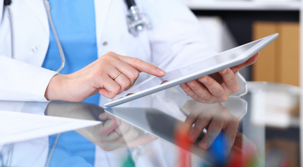 Woman doctor using tablet computer while standing straight in hospital office, closeup. Healthcare, insurance and medicine concept
