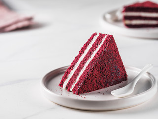 Piece of red velvet cake with perfect texture in matte plate on white marble tabletop. Slice of...