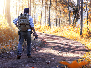 Young man with backpack and holding a binoculars walking on trail in forest