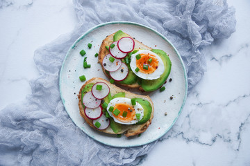 Healthy breakfast, Toasts with avocado, egg, radish, sweet onions, Diet food, On a light marble background, Selective focus, Top view