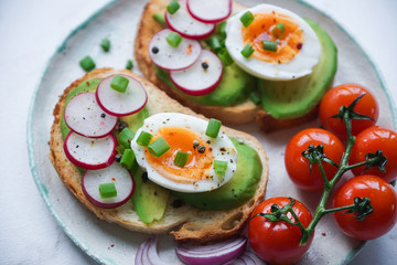 Healthy breakfast, Toasts with avocado, egg, radish, sweet onions and tomatoes, Diet food, On a light marble background, Selective focus closeup