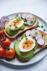 Healthy breakfast, Toasts with avocado, egg, radish, sweet onions and tomatoes, Diet food, On a light marble background, Selective focus closeup