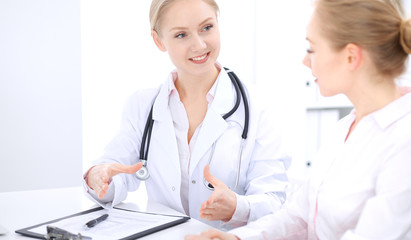Fototapeta premium Blonde female doctor and patient talking in hospital office. Health care and client service in medicine