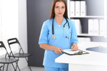 Doctor woman at work. Portrait of female physician filling up medical form while standing near...