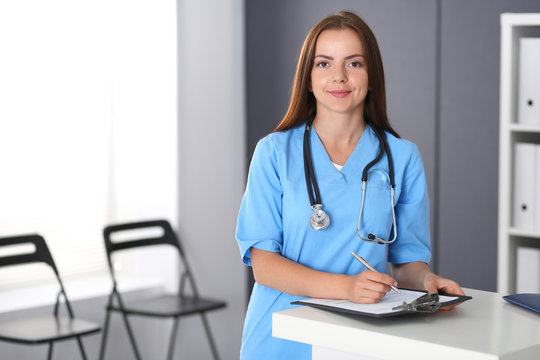 Doctor woman at work. Portrait of female physician filling up medical form while standing near reception desk at clinic or emergency hospital. Medicine and healthcare concept