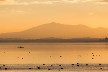 Beautiful view of a lake at sunset, with orange tones, birds on water and a man on a canoe