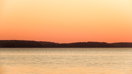 Fototapeta premium Beautiful view of lake at sunset. Orange landscape and silhouette of forest. Copy space.