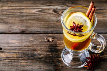 Hot spiced Apple cider Toddy with lemon, honey and cinnamon stick in glass on wooden background