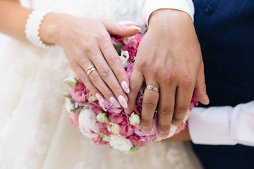 Close-up of the hands of the newlyweds with wedding rings, gently touch the wedding bouquet of peonies.