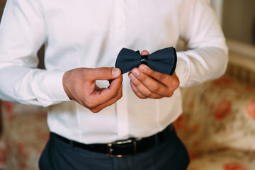 Close-up of a cropped frame of a stylish business man going to a wedding. A businessman in a snow-white shirt dresses a bow tie, wears a fashionable suit, a leather belt.