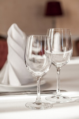 Two empty wine glasses on a served table. White tablecloth, glasses, plates, appliances, red furniture