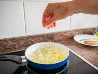 Hand seasoning with salt fried onions in pan on kitchen. Spanish omelet recipe