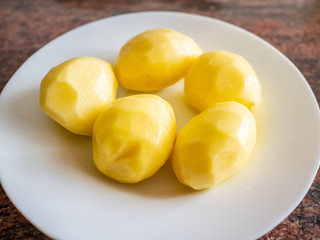 Top view of peeled raw potatoes on white plate in kitchen