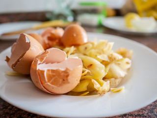Closeup of potato peels and eggs rinds on white table with other ingredients on background