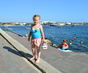 girl standing barefoot on the shore against the sea landscape holding sandals in her hand 