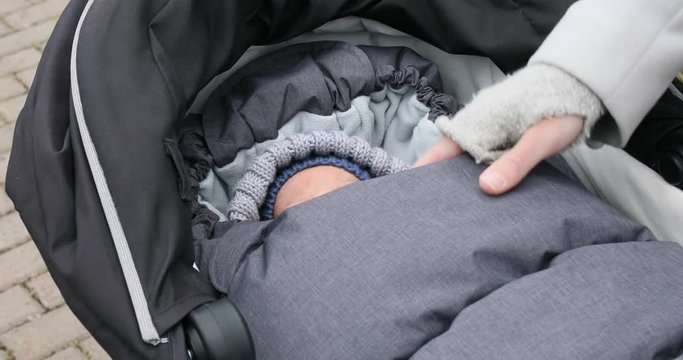 Newborn baby boy sleep in stroller at cold autumn weather in the park