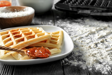 Plate with delicious waffles and jam on wooden table