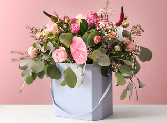 Gift box with beautiful flowers on table against color background