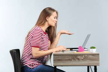 Young woman having online dating while sitting at table with laptop against grey background