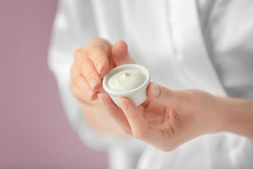 Woman holding bowl with body cream on color background, closeup