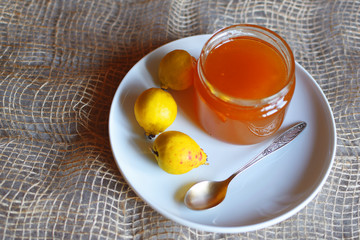 Honey in glass jar spoon and three fresh  yellow quince fruits on white plate on linen cloth background.