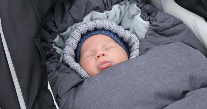 Newborn baby boy sleep in stroller at cold autumn weather in the park