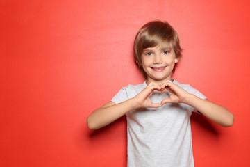 Little boy in t-shirt making heart with his hands on color background