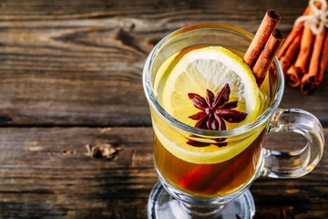 Hot spiced Apple cider Toddy with lemon, honey and cinnamon stick in glass on wooden background