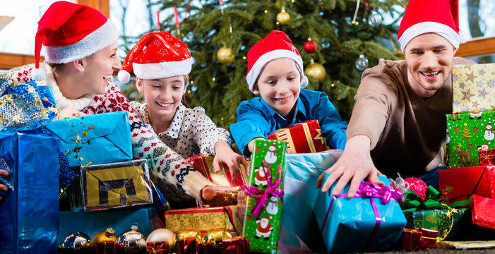 Mum, dad and sons on X-mas during handing out of presents under Christmas tree