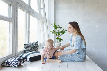 Cute little teddy boy spend joyfully time with mom. Cheerful expectant mother has maternity leave, spends free time with her son, sits against cozy home interior with large window. Family, daylight
