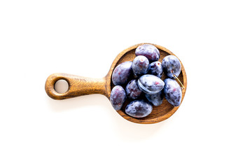 Plums on dinning table. Fresh raw purple plum in wooden bowl on white background top view space for text