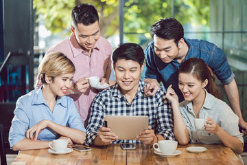 Group of smiling friends looking at digital tablet sitting in the coffee shop