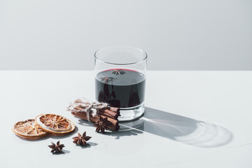 mulled wine in glass, cinnamon sticks and dried oranges on white tabletop