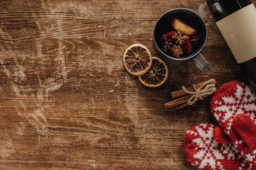 top view of mulled wine in cup, mittens and wine bottle on wooden table, christmas concept