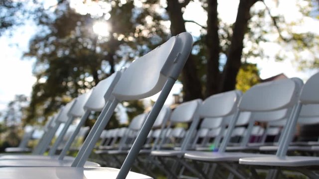 Dynamic shot of white folding chairs outside with sun shining through trees.mov
