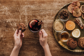 cropped image of woman holding cup of mulled wine and cookie at wooden table