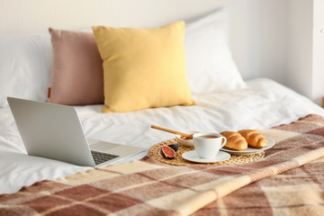 Fototapeta na wymiar Wicker mat with delicious breakfast and laptop on bed