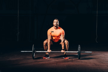 Fototapeta na wymiar handsome athletic bodybuilder lifting barbell in dark gym