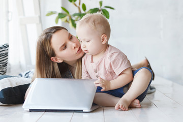 Child upbringing and work. Little lonely child asks her mother to finish her job, closed her laptop and advises mom to play along with him. No time for classes with child. Daylight home scene interior